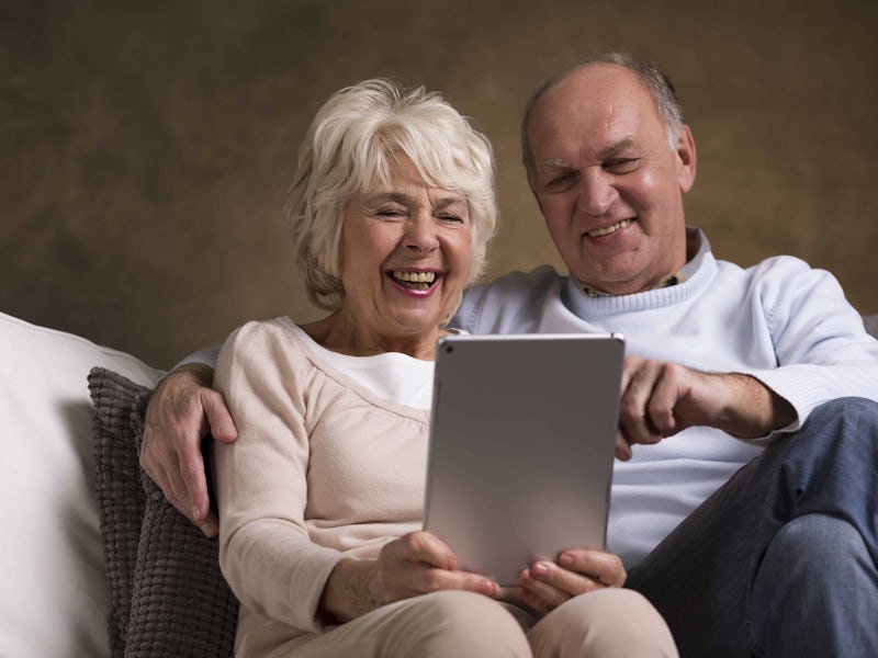 Elderly couple sat together on the sofa using a tablet and both smiling