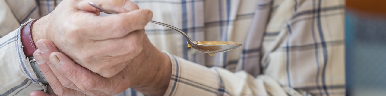 Elderly man with Parkinsons disease holds spoon in both hands eating soup
