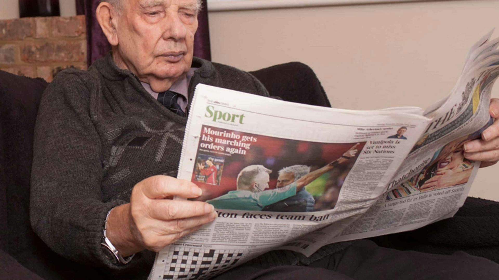 Elderly man sat in a seat reading a newspaper