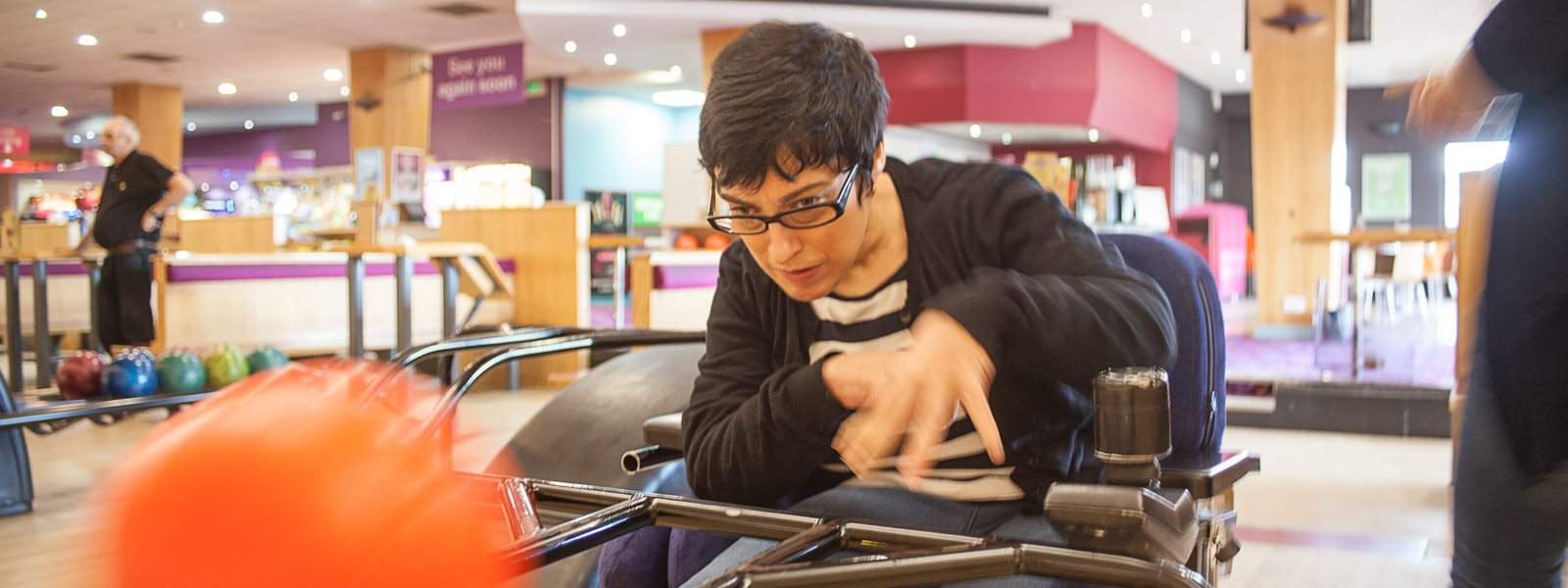 Woman with cerebral palsy in wheel chair with bowling ball at bowling alley