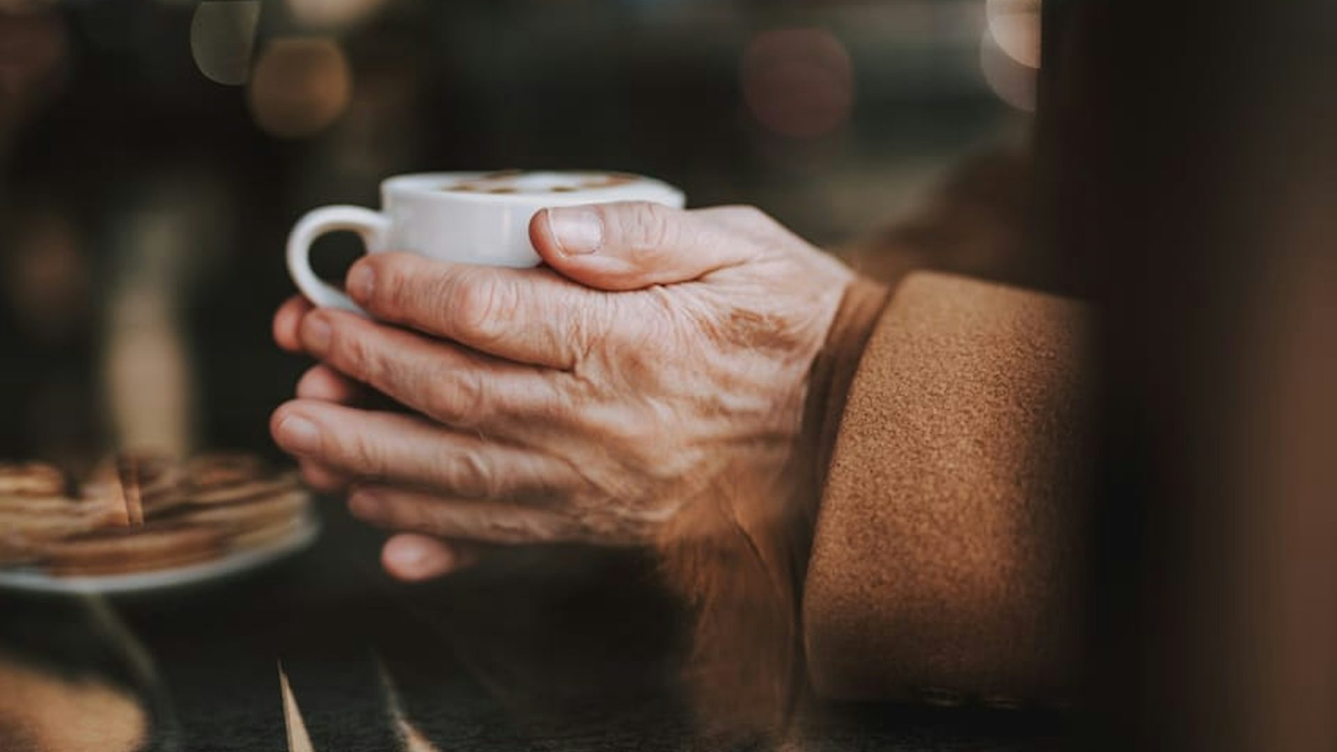Elderly person holding a warm drink in a cup, trying to stay warm