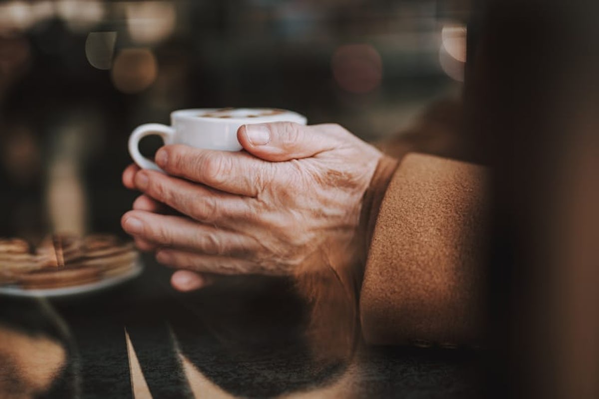 Elderly person holding a warm drink in a cup, trying to stay warm