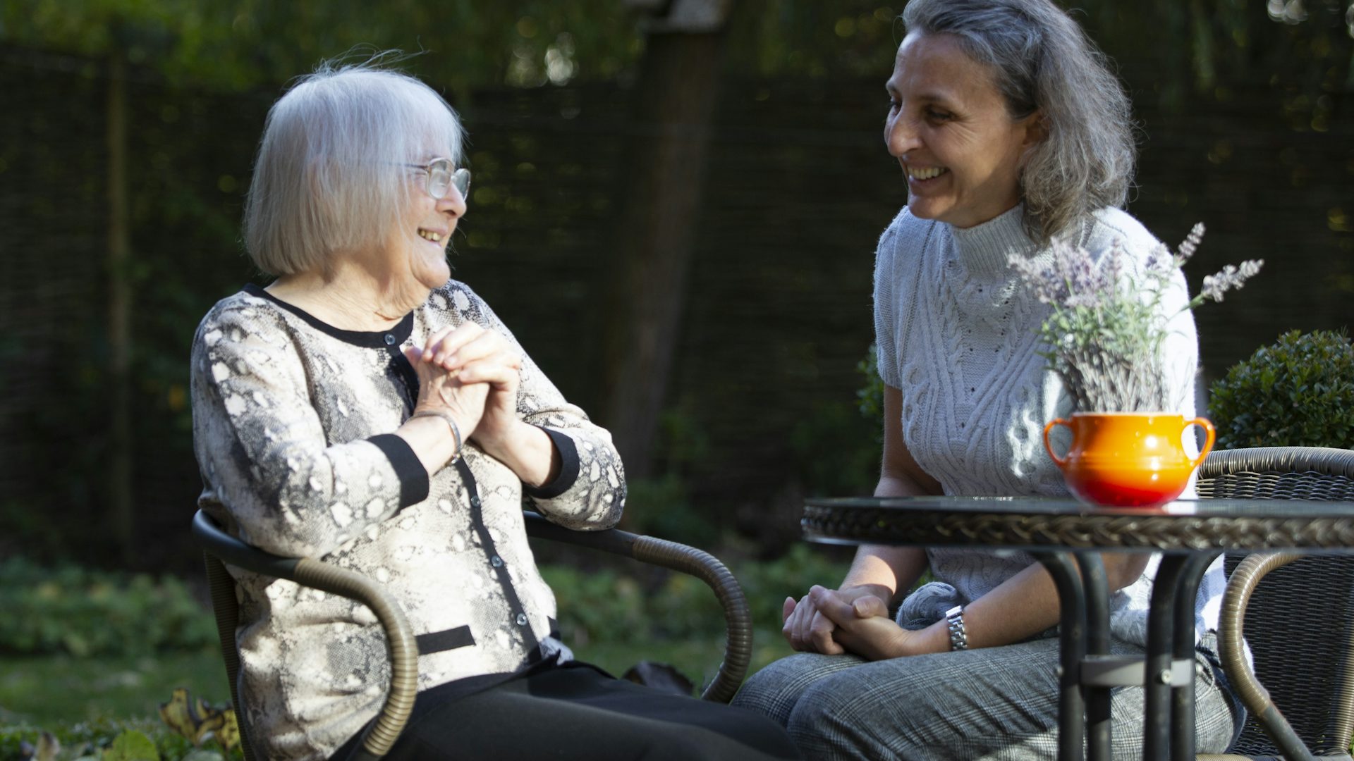 Two women sitting at an outside table talking and laughing.