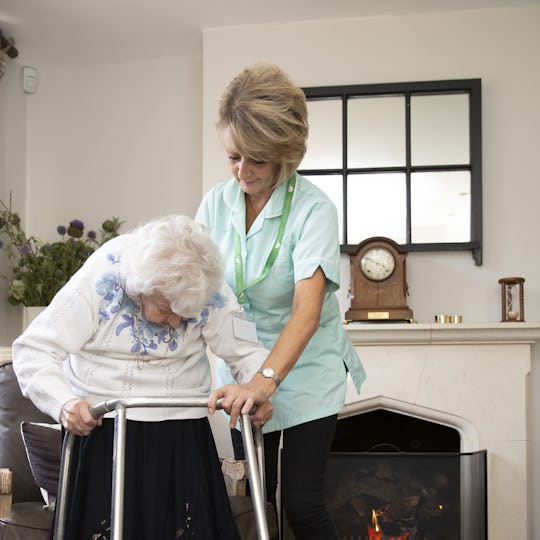 Carer supporting while elderly person is using a walking frame