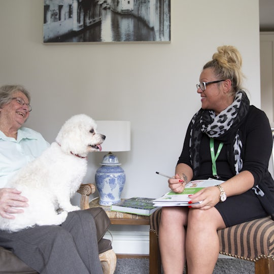 Elderly Lady sat in a chair with her per dog on her lap talking to a care manager